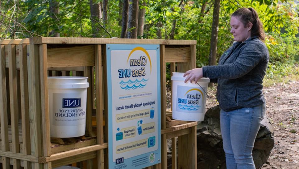 A U N E student dropping off a bucket at the Clean Seas U N E area